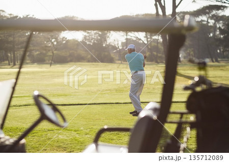 Senior male golfer swinging club on fairway wearing light blue polo and white cap, copy space 135712089