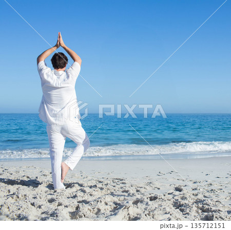Man practicing tree yoga pose on sandy shoreline with ocean waves in white linen outfit Man practicing tree yoga pose on sandy shoreline with ocean waves in white linen outfit 135712151