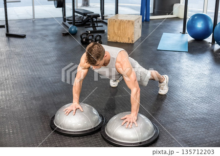 Male in sportswear performing push-up on half-sphere balance trainers on gym floor with kettlebells Male in sportswear performing push-up on half-sphere balance trainers on gym floor with kettlebells 135712203