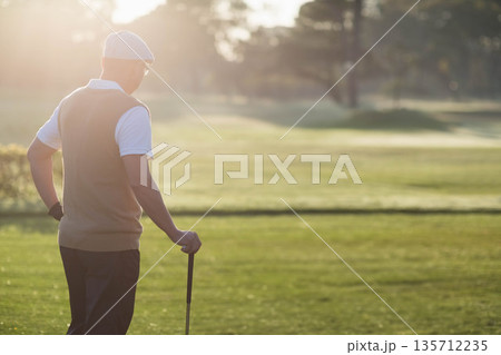 Senior Chinese man standing on verdant fairway at dawn wearing golf attire, gripping golf club Senior Chinese man standing on verdant fairway at dawn wearing golf attire, gripping golf club 135712235