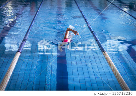 Senior female swimmer gliding through tiled pool lane by lane ropes in pink swim cap goggles 135712236