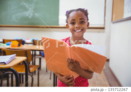 African American child smiling and holding open orange folder while standing in primary classroom African American child smiling and holding open orange folder while standing in primary classroom 135712267