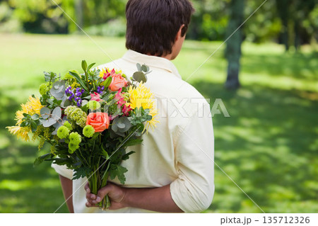 Man standing holding bouquet behind back in park with roses, mums, button poms and eucalyptus Man standing holding bouquet behind back in park with roses, mums, button poms and eucalyptus 135712326