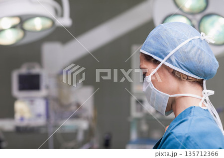Mid adult female nurse monitoring vitals on monitors under surgical lights in OR, copy space 135712366