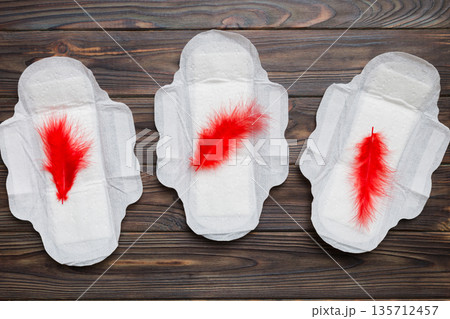 Women hygiene products or Sanitary pad with red feather on colored background. Pastel color. Closeup. Empty place for text. Female daily hygiene Women hygiene products or Sanitary pad with red feather on colored background. Pastel color. Closeup. Empty place for text. Female daily hygiene 135712457