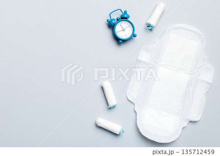 Ringing alarm clock with sanitary female tampons and menstrual sanitary pads. Medical concept of woman critical days and menstruation. Female daily hygiene. Copy space Ringing alarm clock with sanitary female tampons and menstrual sanitary pads. Medical concept of woman critical days and menstruation. Female daily hygiene. Copy space 135712459