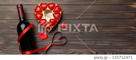 Bottle of red wine on colored background for Valentine Day with gift and chocolate. Heart shaped with gift box of chocolates top view with copy space 135712471