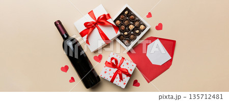 Bottle of red wine on colored background for Valentine Day with gift box, envelope and chocolate. Heart shaped with gift box of chocolates top view with copy space Bottle of red wine on colored background for Valentine Day with gift box, envelope and chocolate. Heart shaped with gift box of chocolates top view with copy space 135712481