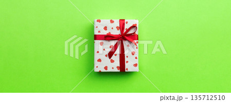 Gift box with red ribbon and heart on green background, top view with copy space for text 135712510