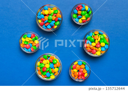 different colored round candy in bowl and jars. Top view of large variety sweets and candies with copy space different colored round candy in bowl and jars. Top view of large variety sweets and candies with copy space 135712644