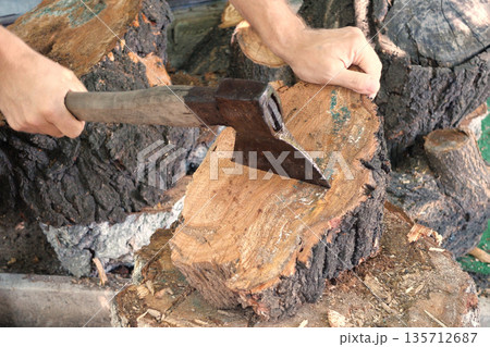 Cutting wood with a large sharp ax, Man Chops firewood, Chopping of wood on a wooden log in summer at the home Cutting wood with a large sharp ax, Man Chops firewood, Chopping of wood on a wooden log in summer at the home 135712687