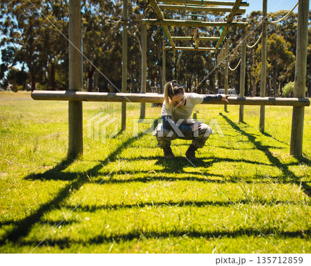 Woman navigating horizontal beam obstacle on wooden posts on grassy field wearing military uniform Woman navigating horizontal beam obstacle on wooden posts on grassy field wearing military uniform 135712859