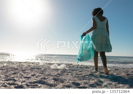 African American woman in green dress walking shore picking debris with turquoise bag, copy space African American woman in green dress walking shore picking debris with turquoise bag, copy space 135712864
