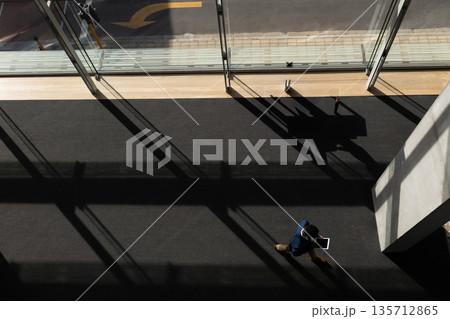 Man walking through carpeted hall toward glass doors under sunlight holding tablet, copy space 135712865