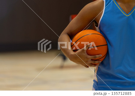 African American male holding orange basketball wearing blue jersey on gym court, copy space African American male holding orange basketball wearing blue jersey on gym court, copy space 135712885