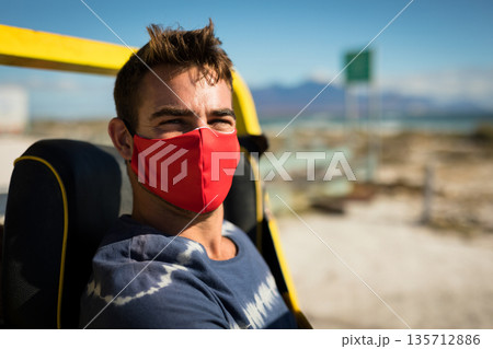 Man sitting on seat frame under yellow roll bar on coastal road wearing red cloth mask 135712886