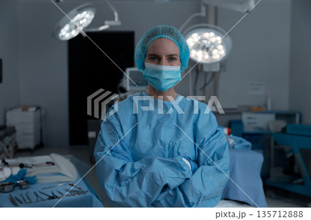 Female surgeon standing in operating room wearing blue gown organizing tools under surgical lights 135712888