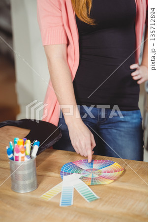 Adult female pointing at printed color wheel on wooden tabletop near fan of swatches and markers 135712894