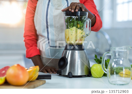 African American female operating blender with leafy greens in home kitchen with halved citrus African American female operating blender with leafy greens in home kitchen with halved citrus 135712903