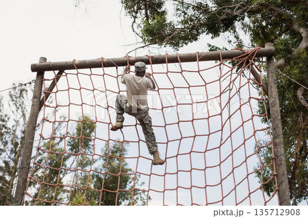 African American male soldier in camo climbing red rope net reaching wooden beam on obstacle course African American male soldier in camo climbing red rope net reaching wooden beam on obstacle course 135712908