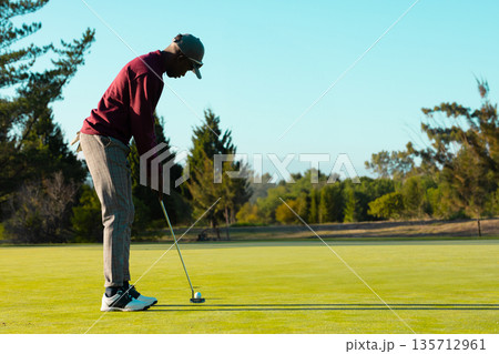 African American man lining up putt on putting green holding putter and ball, copy space 135712961