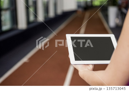 Adult holding tablet and studying track lanes inside sports hall with sunlight filtering Adult holding tablet and studying track lanes inside sports hall with sunlight filtering 135713045