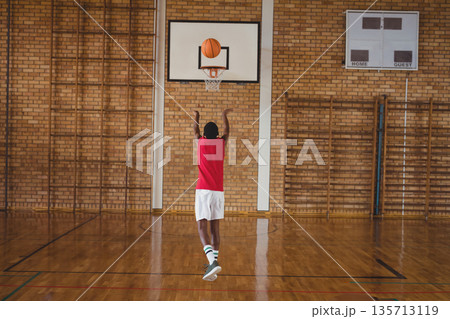 Asian teenage boy shooting basketball toward backboard-mounted hoop at school gym with scoreboard Asian teenage boy shooting basketball toward backboard-mounted hoop at school gym with scoreboard 135713119