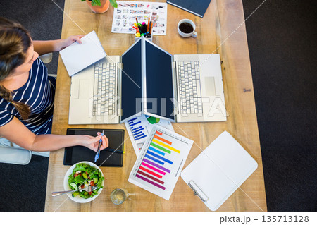 Indian woman working at office workspace while sketching on tablet with laptops, coffee, copy space 135713128