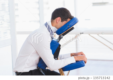Man in business attire sitting on blue massage chair in wellness room leaning forward Man in business attire sitting on blue massage chair in wellness room leaning forward 135713142