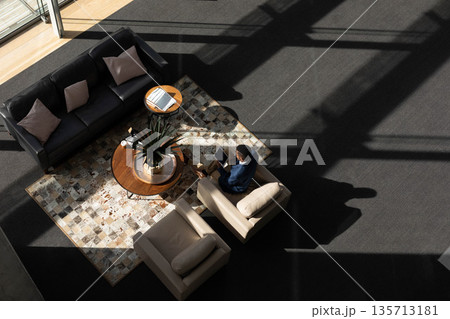 Man sitting on cream armchair wearing business casual and holding tablet in lounge, copy space 135713181