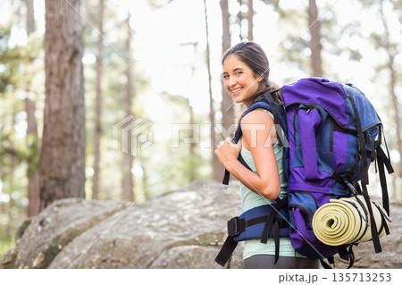 Female hiker standing on rock at pine forest trail carrying backpack and sleeping mat, copy space 135713253