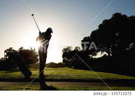 Mature adult male golfer swinging club on tee at golf course with golf bag, copy space 135713272