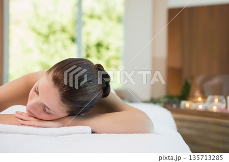 Woman receiving massage on table in spa room wearing white towel beside lit candles on shelf 135713285