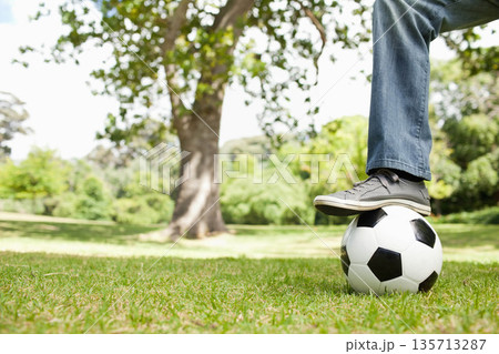 Male balancing foot on soccer ball, wearing denim pants, gray sneakers on park lawn, copy space Male balancing foot on soccer ball, wearing denim pants, gray sneakers on park lawn, copy space 135713287