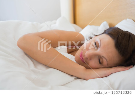Woman sleeping peacefully on bed with pillow and duvet beside headboard in bedroom, copy space 135713326