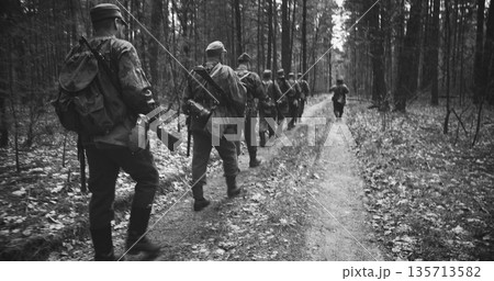 Group Of Reenactors Dressed As German Infantry Soldiers Marching By Forest Road Autumn Season. Reenactment Tactic Game. Wermacht German Military Uniform And Rifle During Ww2. Carabin Mauser 98k. Black Group Of Reenactors Dressed As German Infantry Soldiers Marching By Forest Road Autumn Season. Reenactment Tactic Game. Wermacht German Military Uniform And Rifle During Ww2. Carabin Mauser 98k. Black 135713582