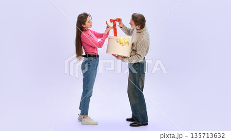 Couple opening small gift together with large box during Valentine celebration Couple opening small gift together with large box during Valentine celebration 135713632