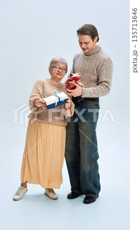 Young man and elderly woman exchanging gift boxes together. Young man and elderly woman exchanging gift boxes together. 135713646