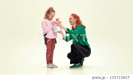 Woman giving gift box to young girl with joyful surprise. Woman giving gift box to young girl with joyful surprise. 135713657