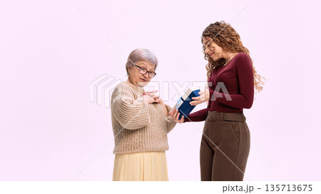 Young woman giving wrapped present to elderly woman with gratitude. 135713675