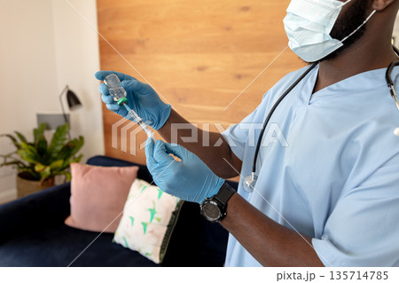 African American male wearing scrubs, stethoscope filling syringe via vaccine vial home, copy space 135714785