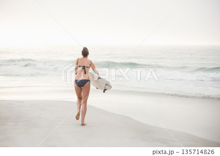 Female surfer walking toward shoreline on sandy beach in polka-dot bikini carrying white surfboard Female surfer walking toward shoreline on sandy beach in polka-dot bikini carrying white surfboard 135714826