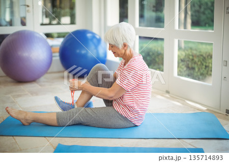 Senior woman stretching on blue exercise mat in home gym with stability balls, copy space 135714893