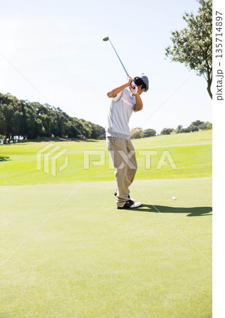 Asian man swinging golf club on putting green at golf course with golf ball and glove 135714897