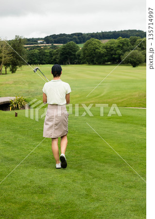 Mature female golfer standing on manicured fairway holding golf club over shoulder Mature female golfer standing on manicured fairway holding golf club over shoulder 135714997