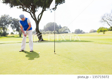 Senior African American golfer lining up putter and ball on putting green by flagstick, copy space 135715072