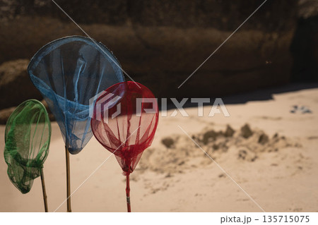 Three multicolored mesh nets are standing in sand on beach near dark rock and sand pile Three multicolored mesh nets are standing in sand on beach near dark rock and sand pile 135715075