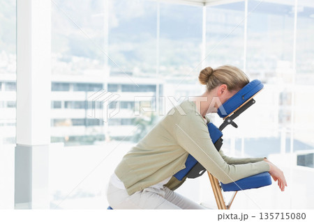 Woman receiving massage while leaning on blue cushioned chair in glass treatment room, copy space Woman receiving massage while leaning on blue cushioned chair in glass treatment room, copy space 135715080