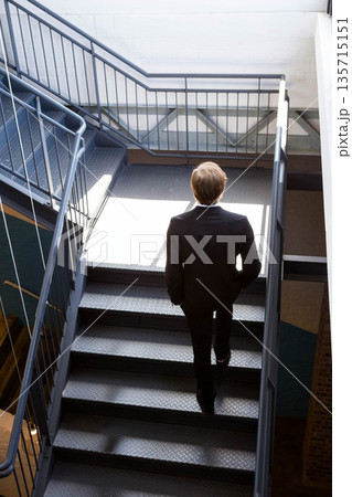 Business male ascending steel staircase with handrails in industrial stairwell lighting white walls Business male ascending steel staircase with handrails in industrial stairwell lighting white walls 135715151