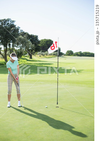 Senior golfer in golf attire aligning putter with ball on putting green hole 18, copy space 135715219